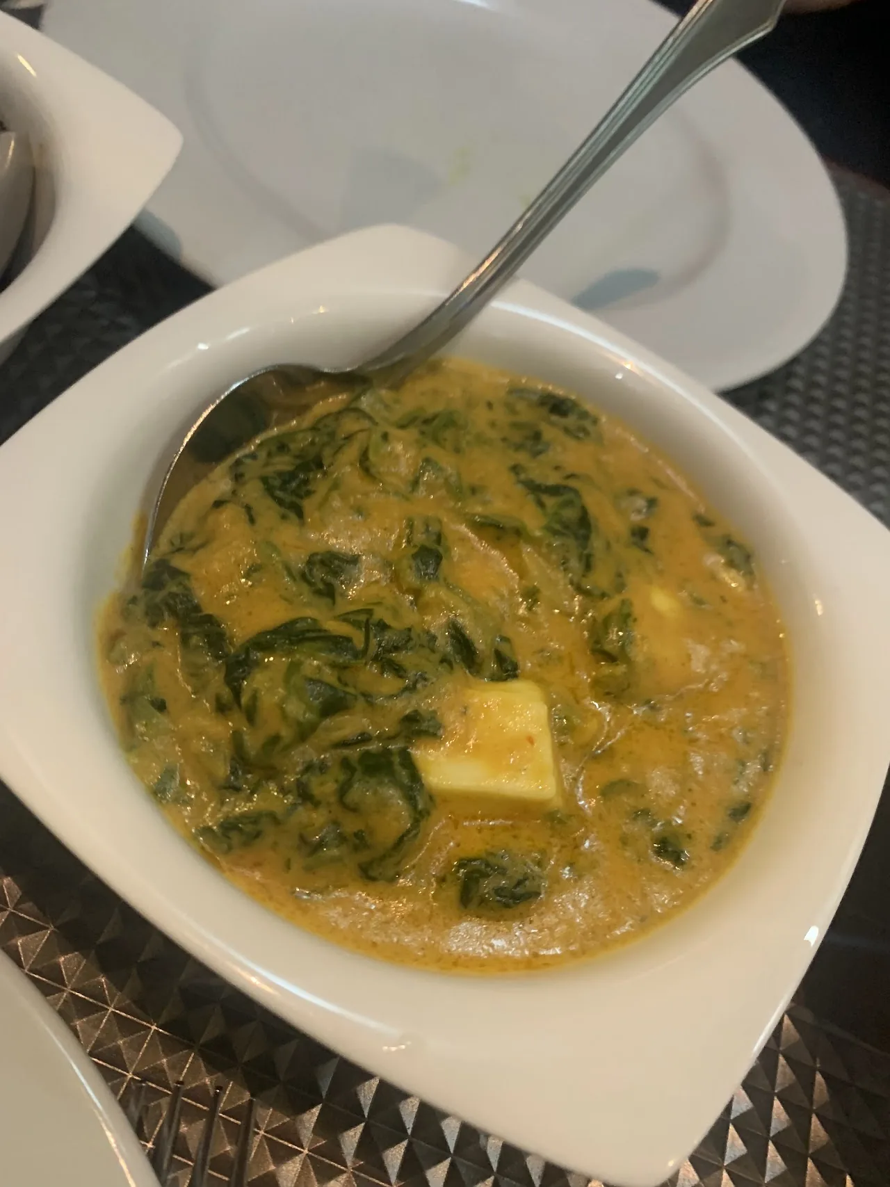 A bowl of creamy spinach curry with a piece of paneer