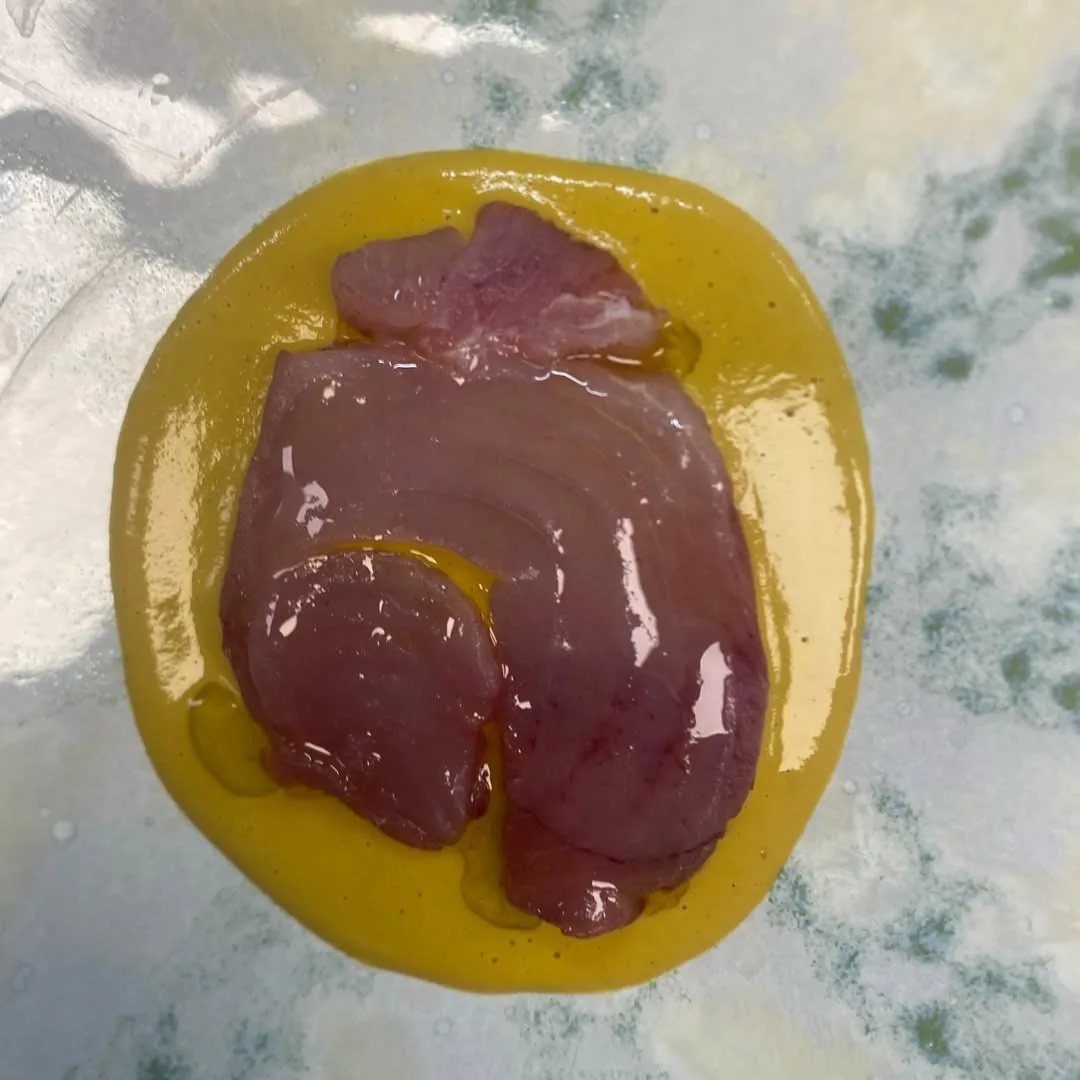 A round piece of raw tuna on a bright yellow sauce
