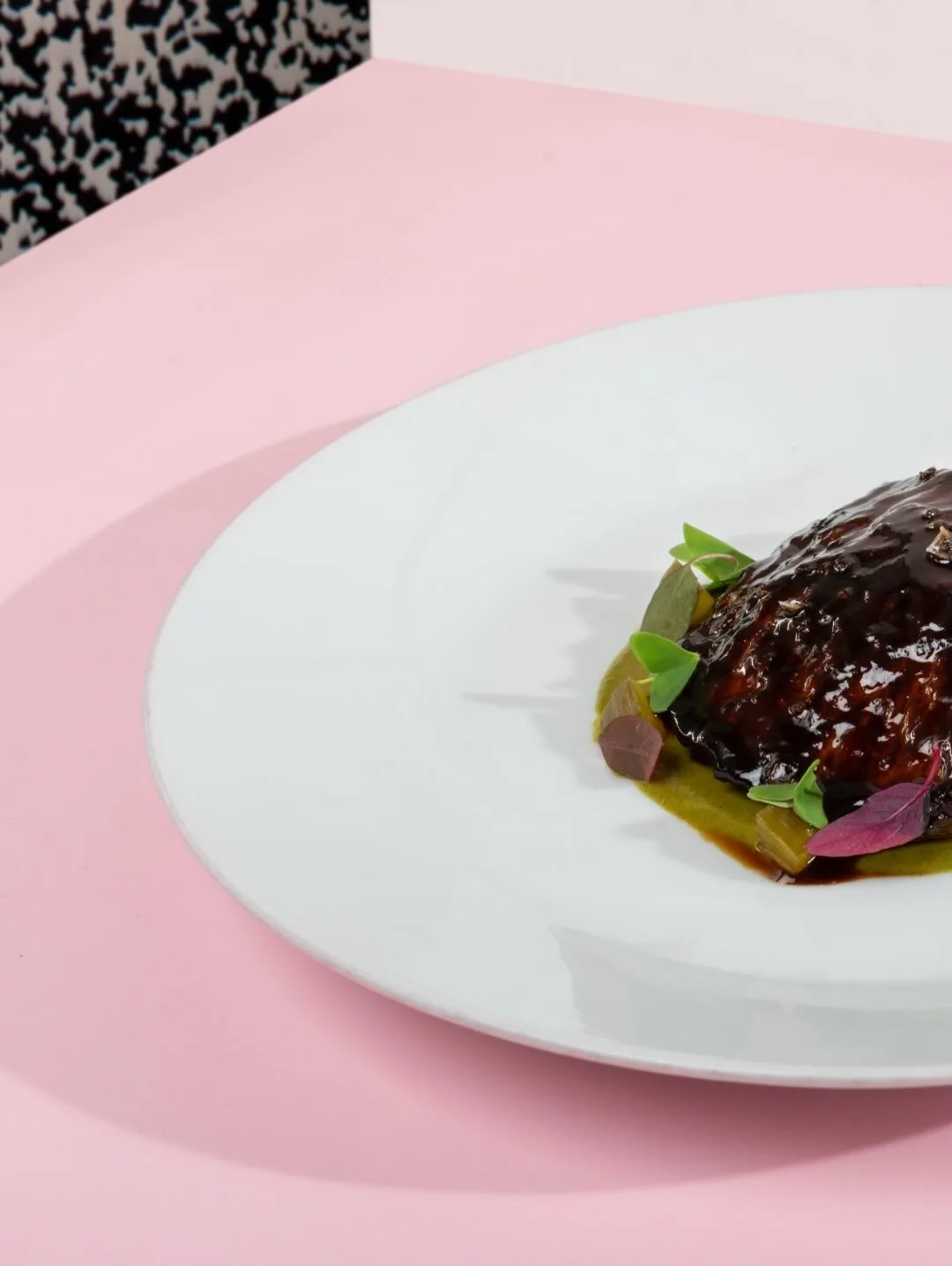 A white plate of a dark glazed dish on a pink tablecloth