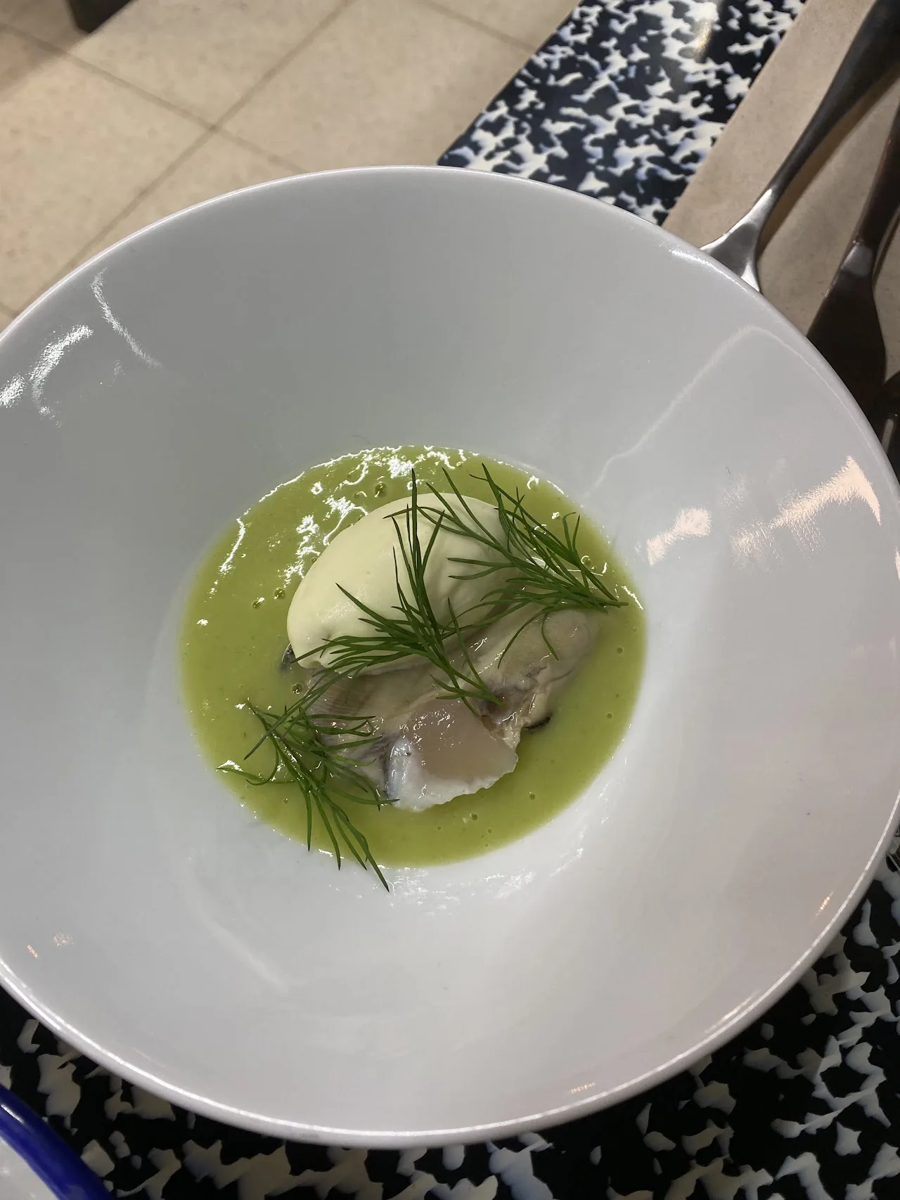 A white bowl of pale green soup with a piece of fish and dill garnish