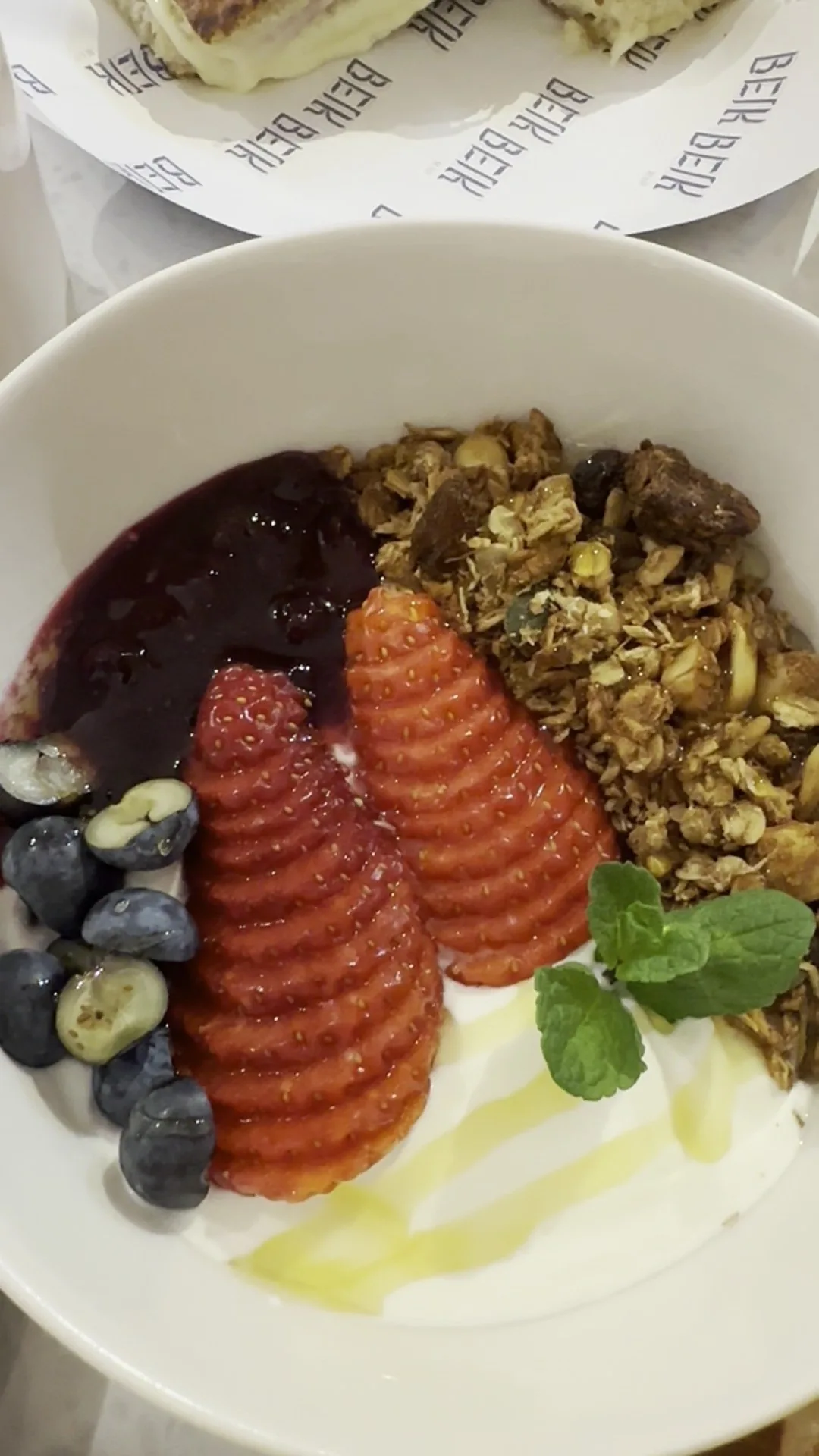 A bowl of yoghurt with granola, blueberries and sliced strawberries
