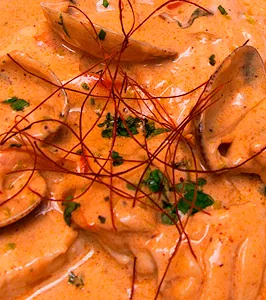 Close-up of pasta parcels and mushrooms in a thick orange cream sauce, scattered with chopped parsley and fine red chilli threads