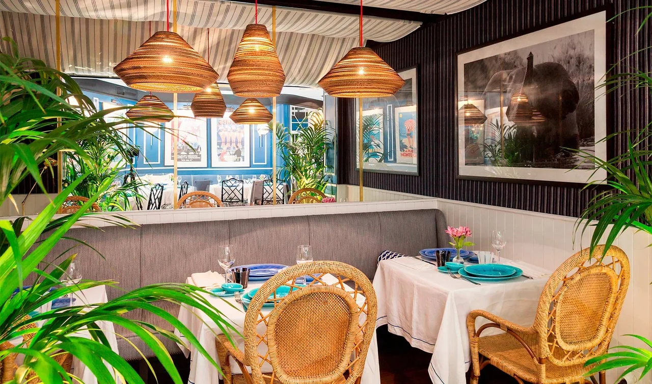 A dining area with a cushioned bench, wicker chairs, plants and hanging lamps