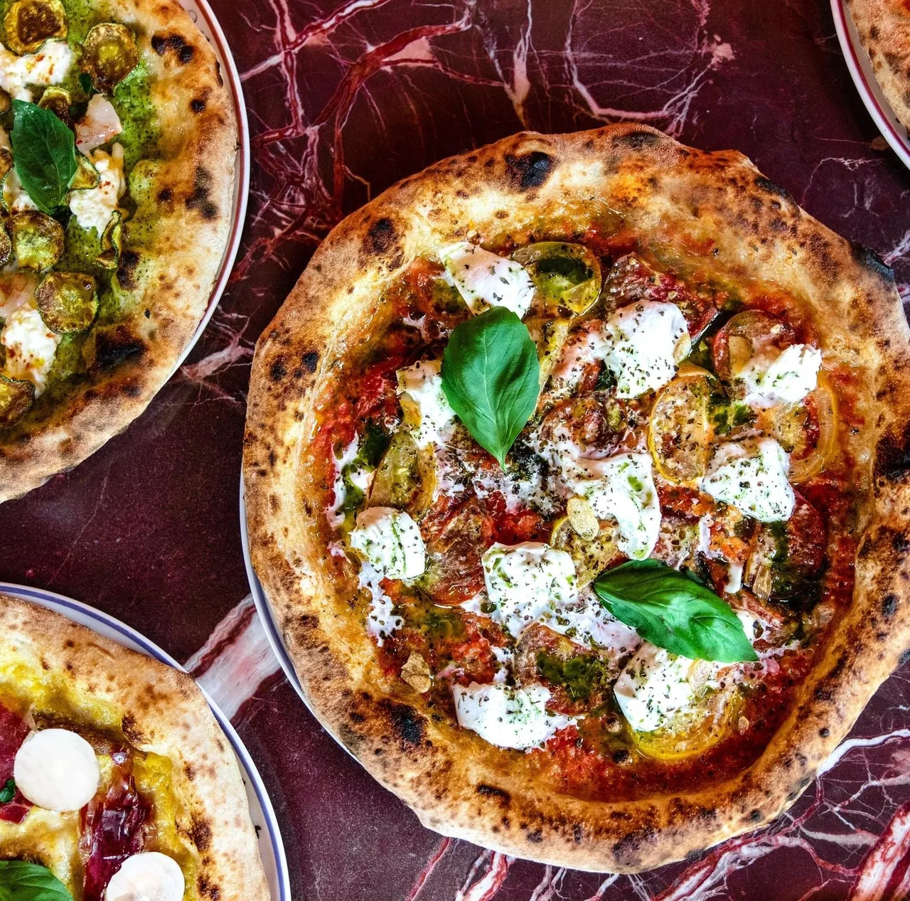 Several round pizzas with basil and white cheese seen from above