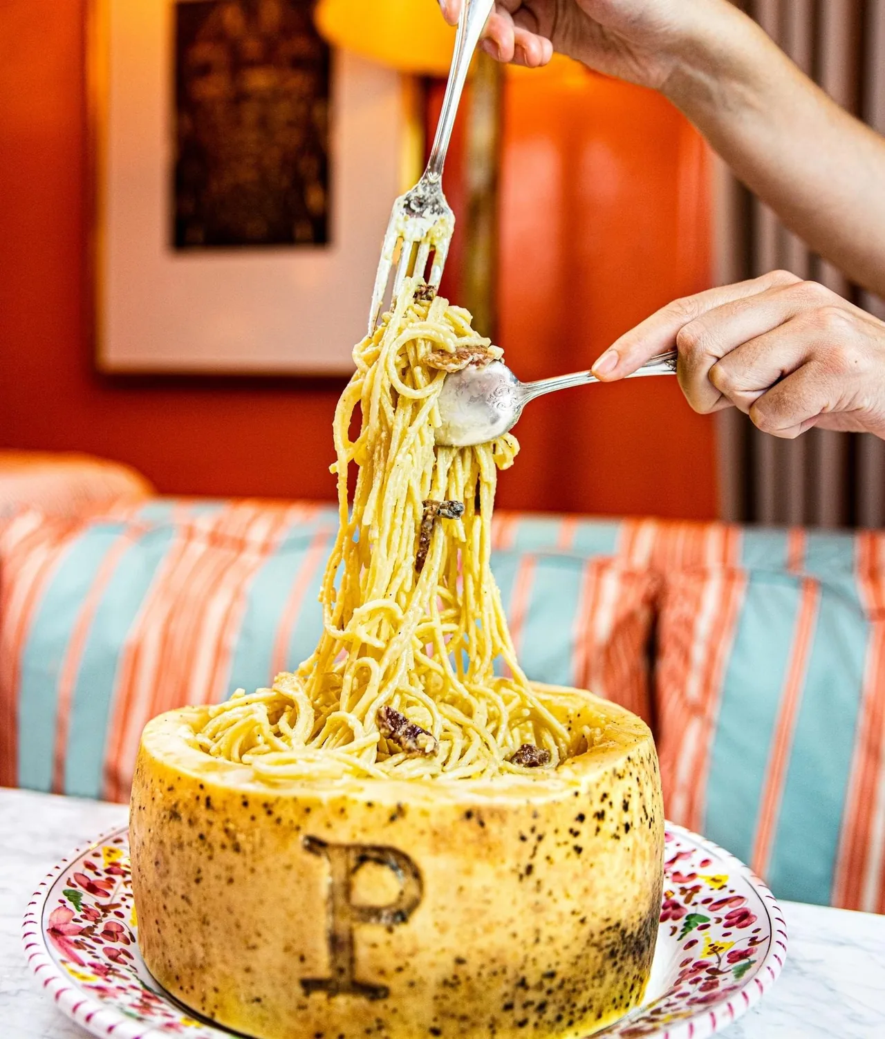 A tower of spaghetti being lifted with a fork from a hollowed round of hard cheese