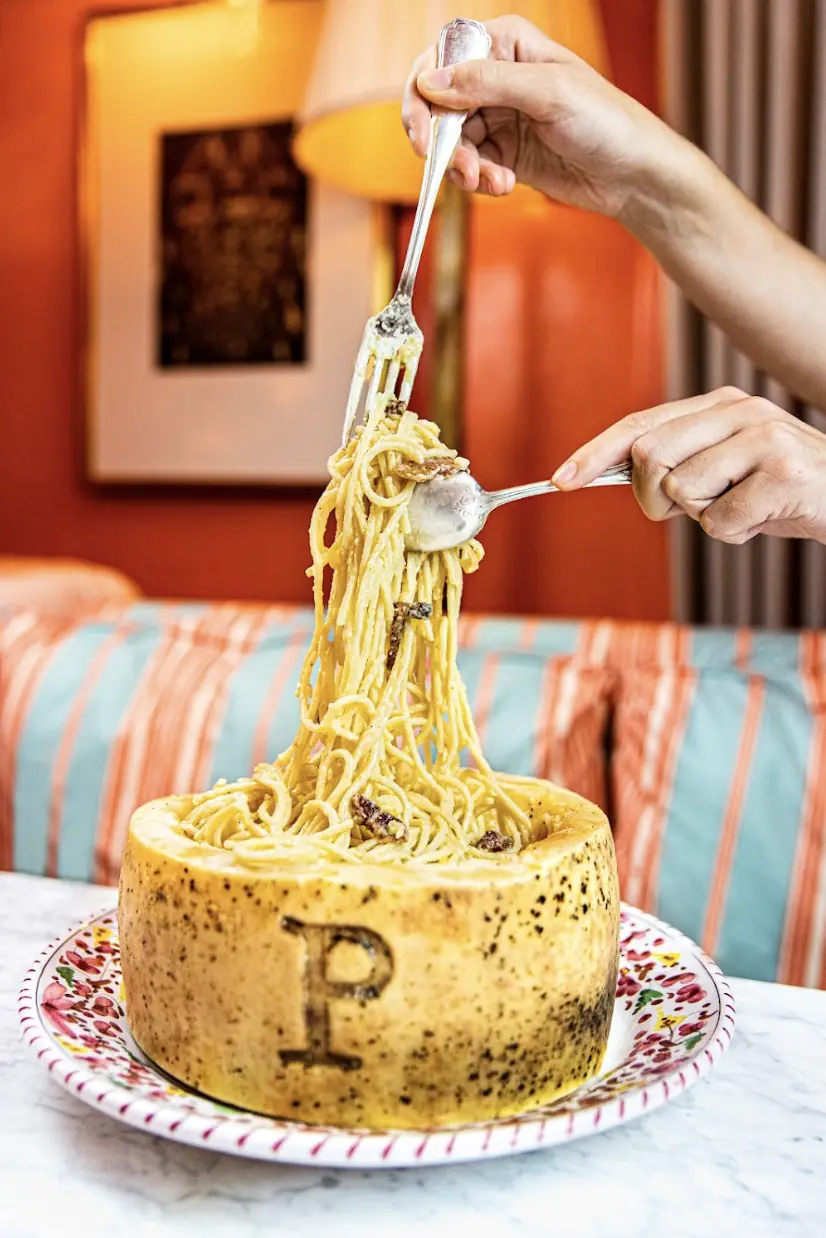 A hand twirling spaghetti tossed tableside in a wheel of cheese.