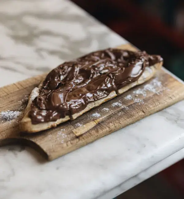 Focaccia flatbread spread thick with melted chocolate-hazelnut cream, dusted with powdered sugar, served on a wooden board at Bella's