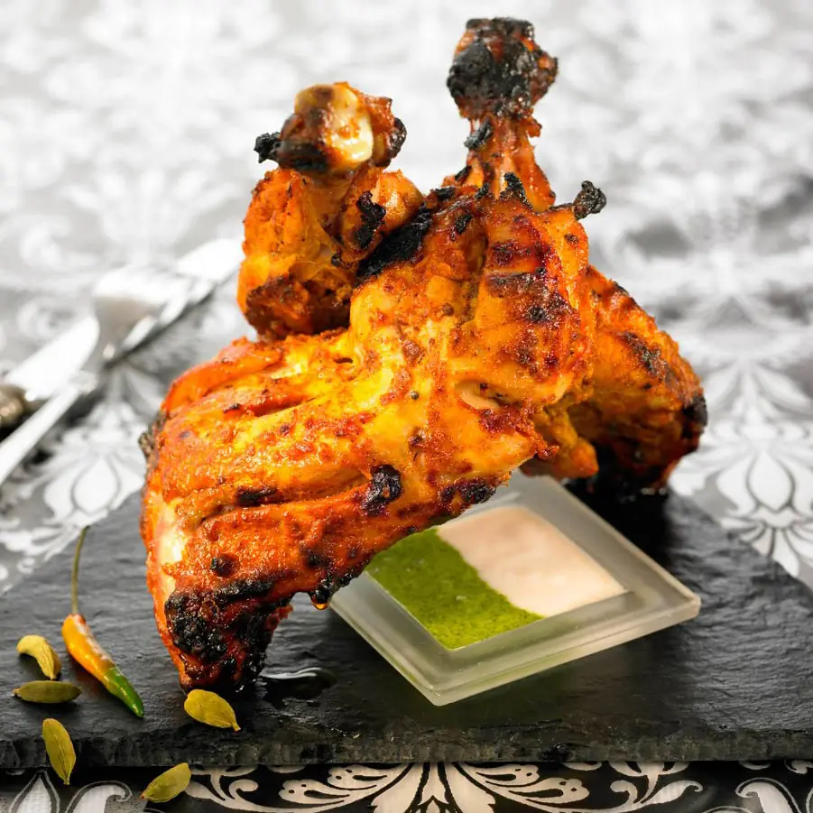 Charred tandoori chicken quarters on a slate board with mint and yogurt dips, at Bembi