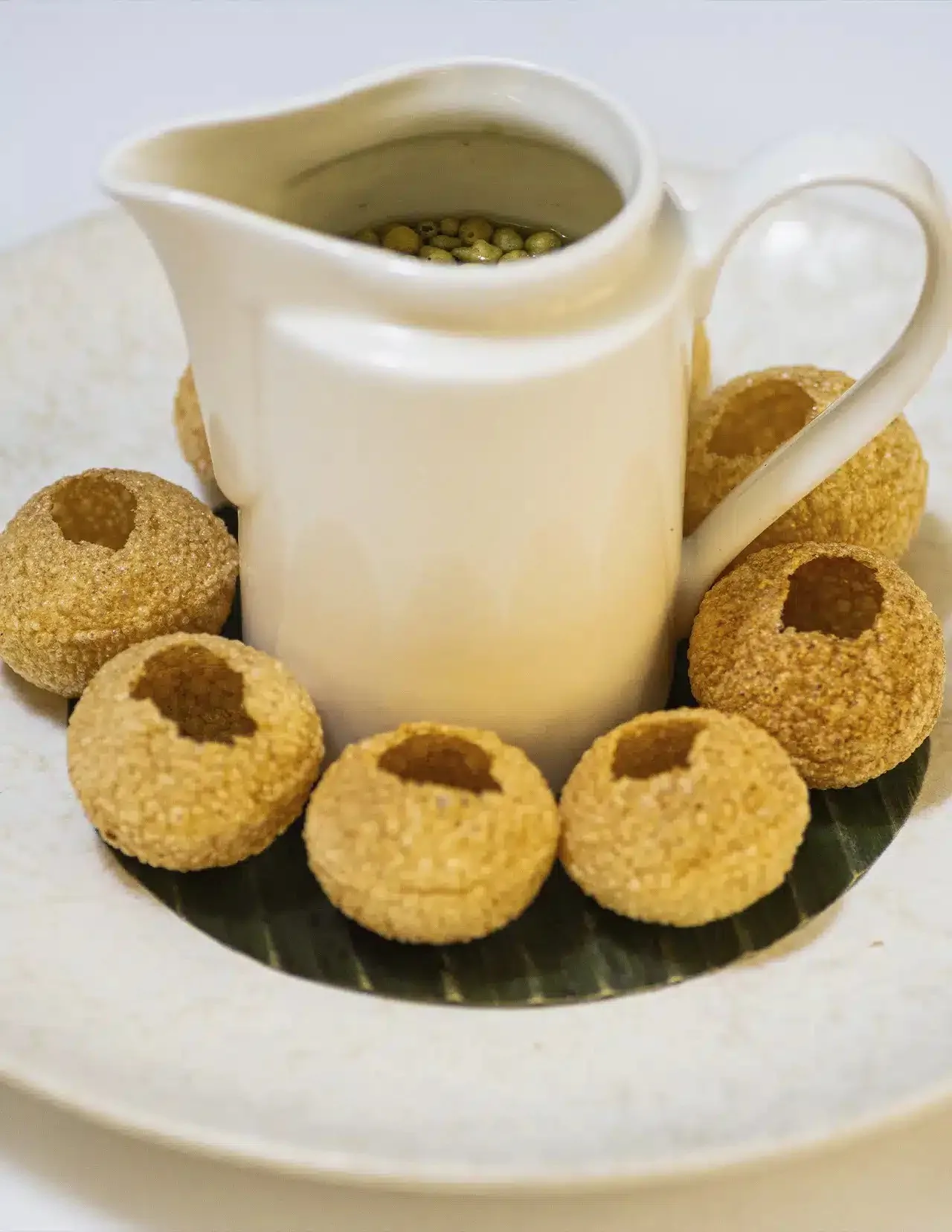 Round crisp shells arranged on a leaf-lined plate with a white jug of liquid