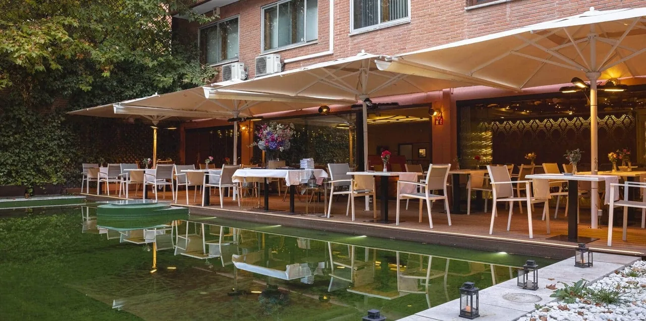 Terrace tables under large white parasols beside a long water feature in a brick-walled garden