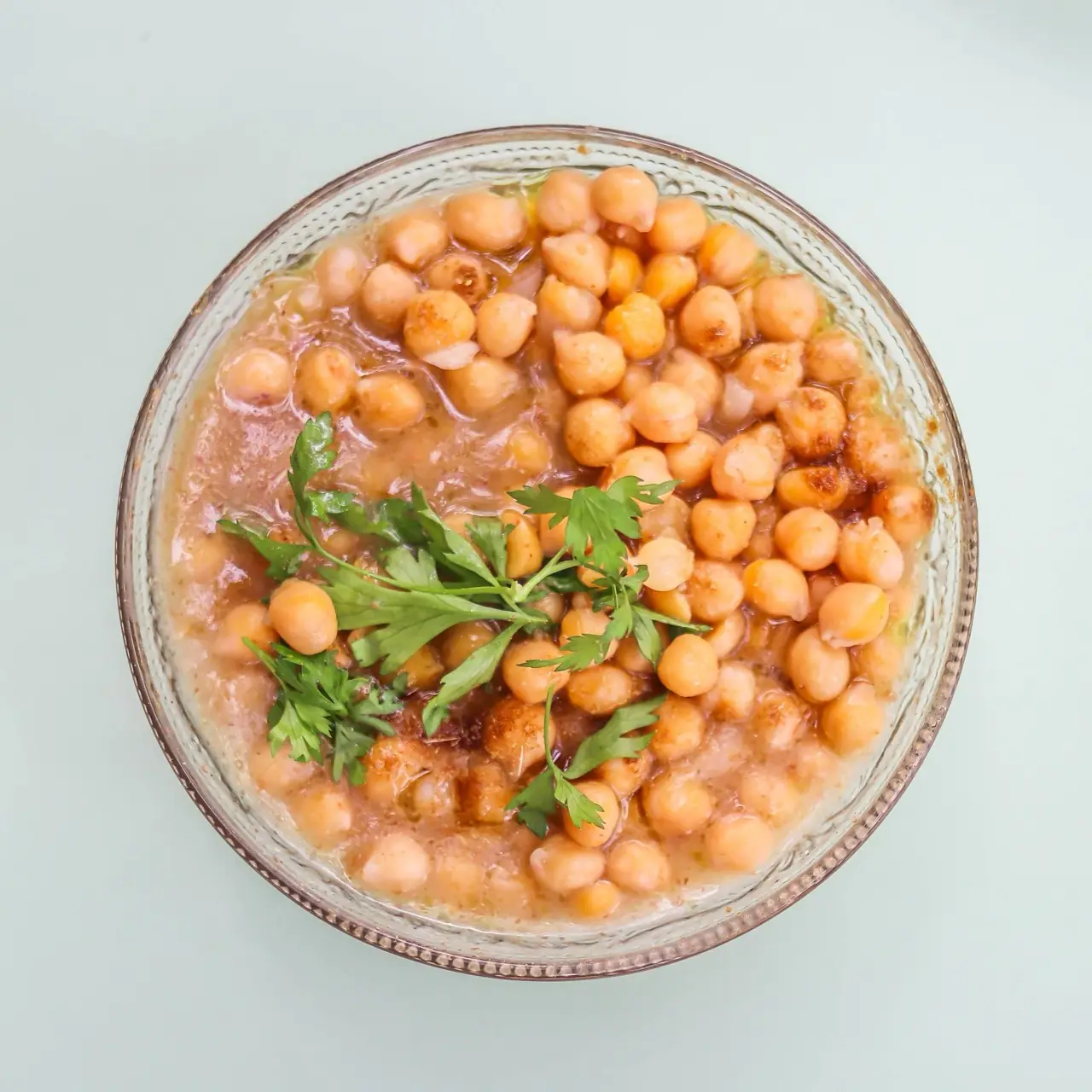 Overhead view of a bowl of stewed chickpeas garnished with fresh parsley, at Bērytī