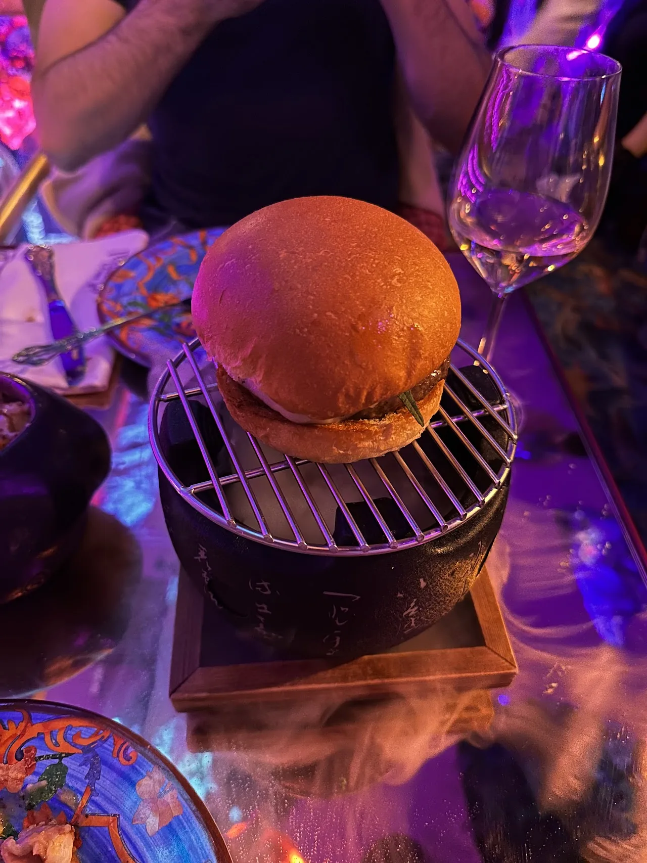 A small burger served on a mini charcoal grill stand