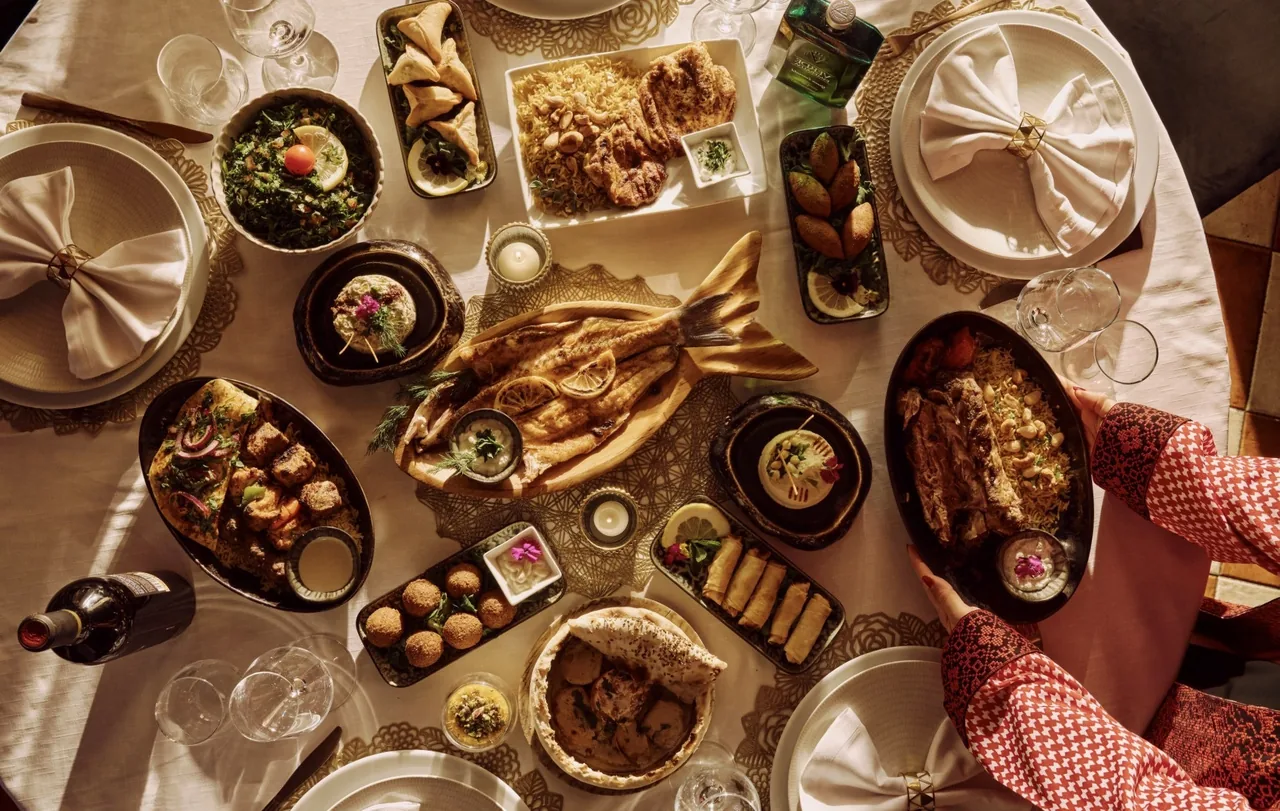 A round table seen from above covered with Middle Eastern dishes including a whole grilled fish, falafel, salads, dips and rice platters