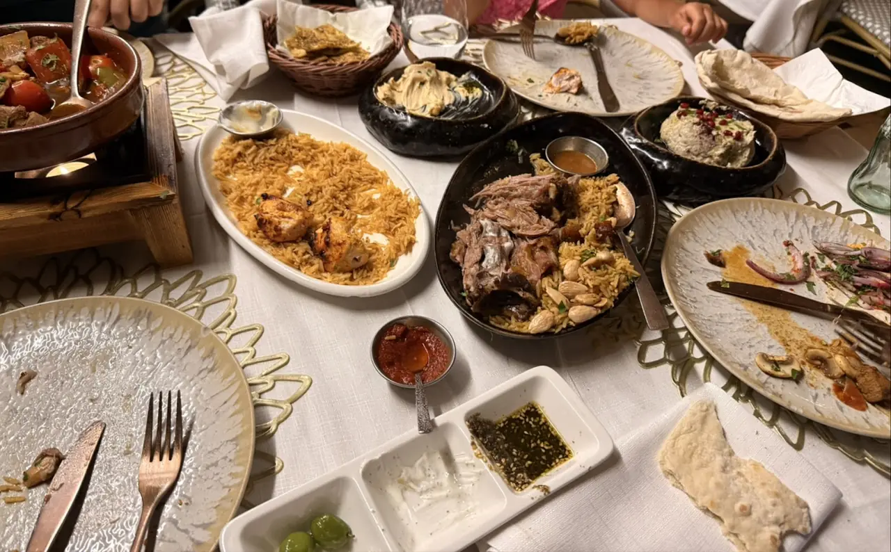 Overhead spread of rice dishes with grilled chicken and lamb, hummus, pita bread and dips on a table