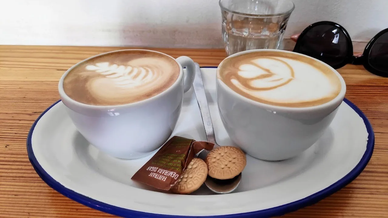 Two cappuccinos with latte art on a white plate with a biscuit, on a wooden table
