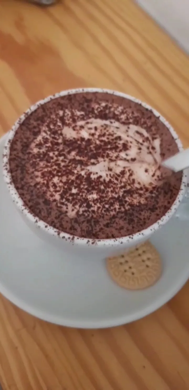 A hot chocolate topped with cream and cocoa powder, served with a cookie