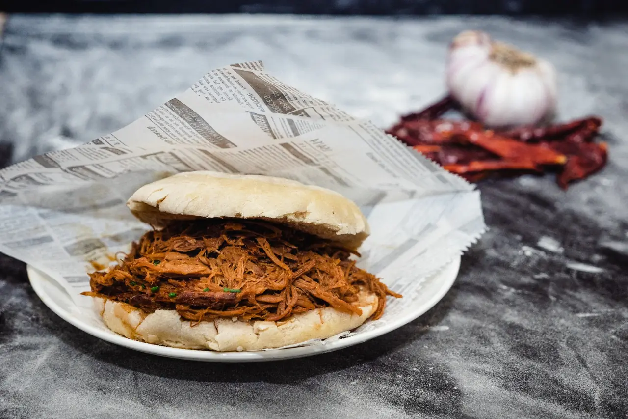 Pulled meat sandwich on a bun wrapped in newspaper, plated