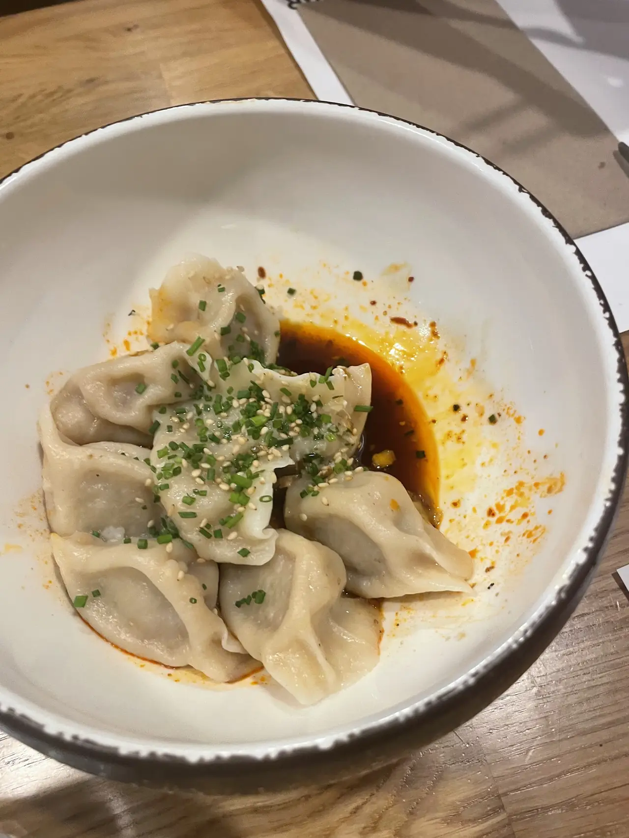 Bowl of dumplings topped with chives and sesame seeds in chili oil sauce