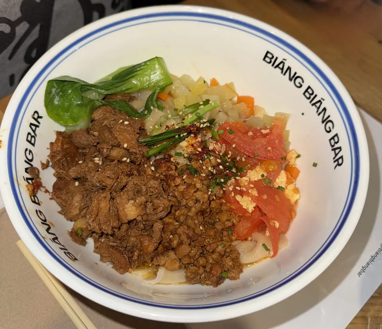 Bowl of noodles with braised meat, minced meat, tomato and bok choy on a Biang Biang Bar plate