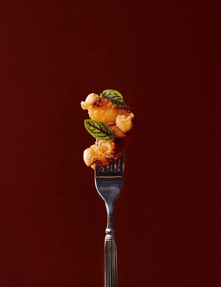 A fork holding a bite of fried food with a herb garnish against a deep red background