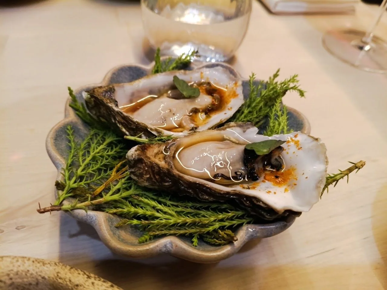 Two oysters on a bed of green sprigs in a scalloped dish