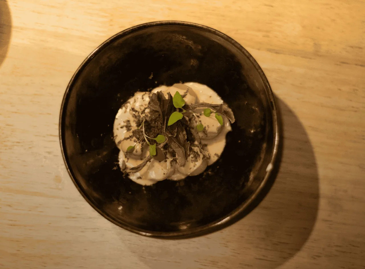 A dark bowl of a creamy white dish with green leaves on a wooden table