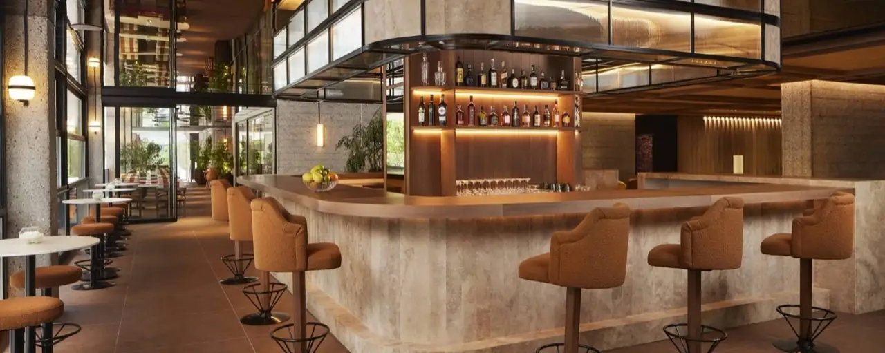 Curved marble bar counter with stocked back-bar shelf of spirits, orange boucle bar stools, empty of patrons.