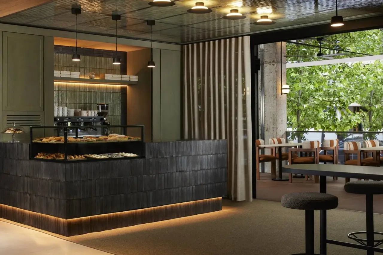 Dark-tiled pastry and sandwich display counter with hanging pendant lights, sliding curtain, and outdoor seating visible through open doorway.