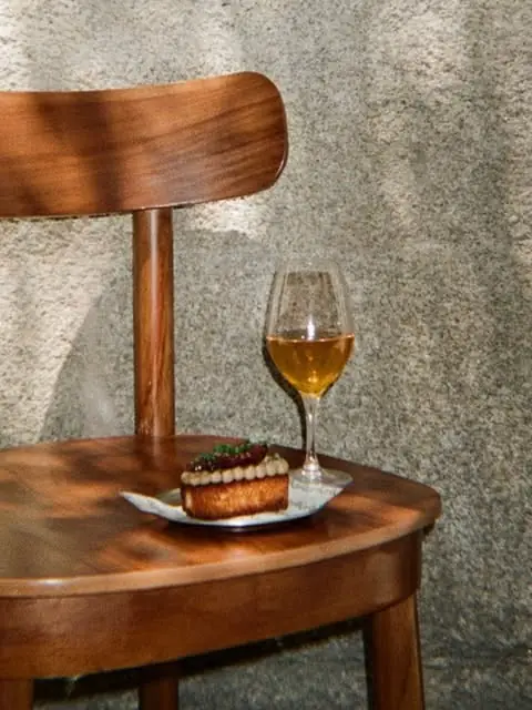 A plated savoury brioche topped with white beans and diced tomato beside a glass of white wine on a wooden bistro chair