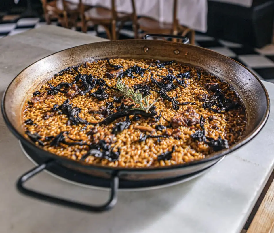 Squid-ink paella with rice and rosemary garnish served in a paella pan at Bistro Mato
