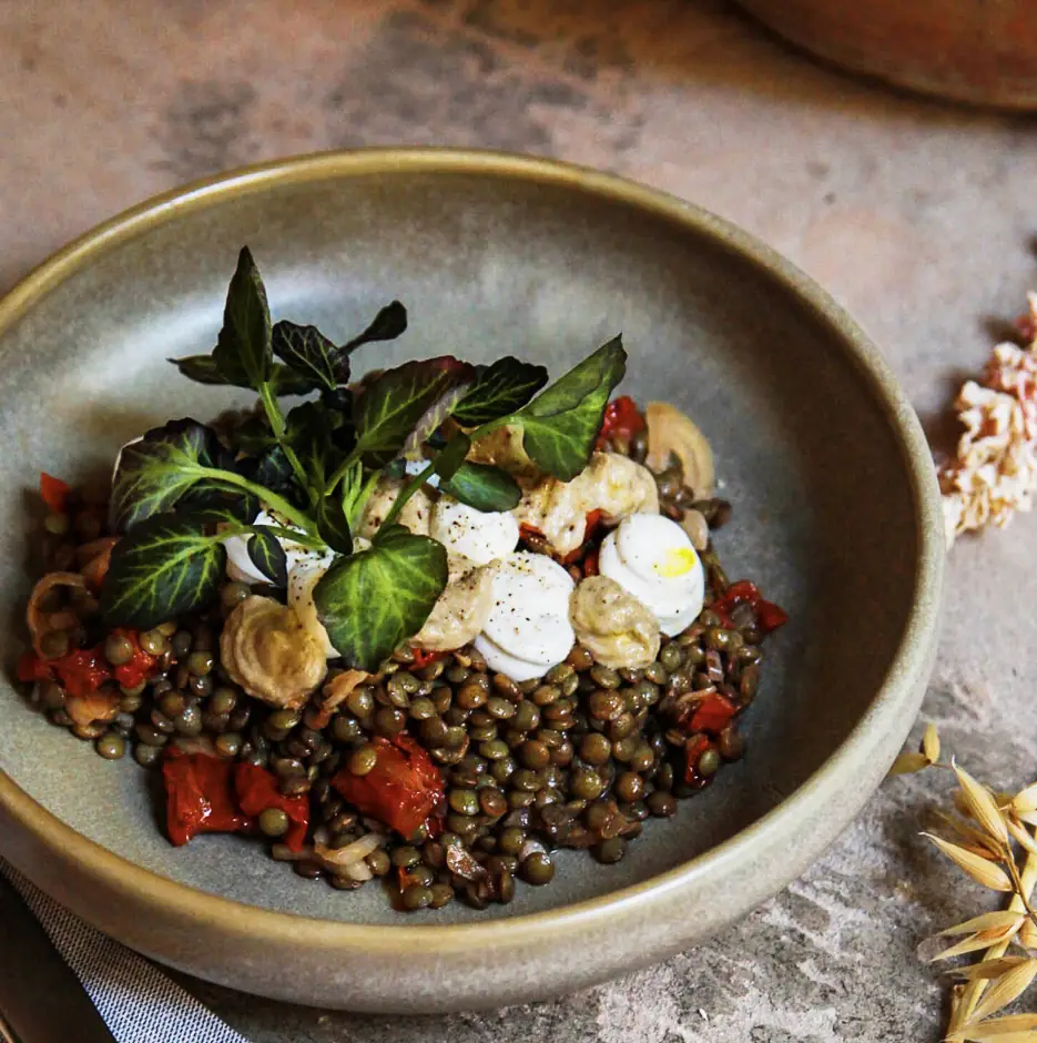 A ceramic bowl of green lentils with roasted red pepper, sliced mushrooms, and fresh herb sprigs on top, Bistrot Levante