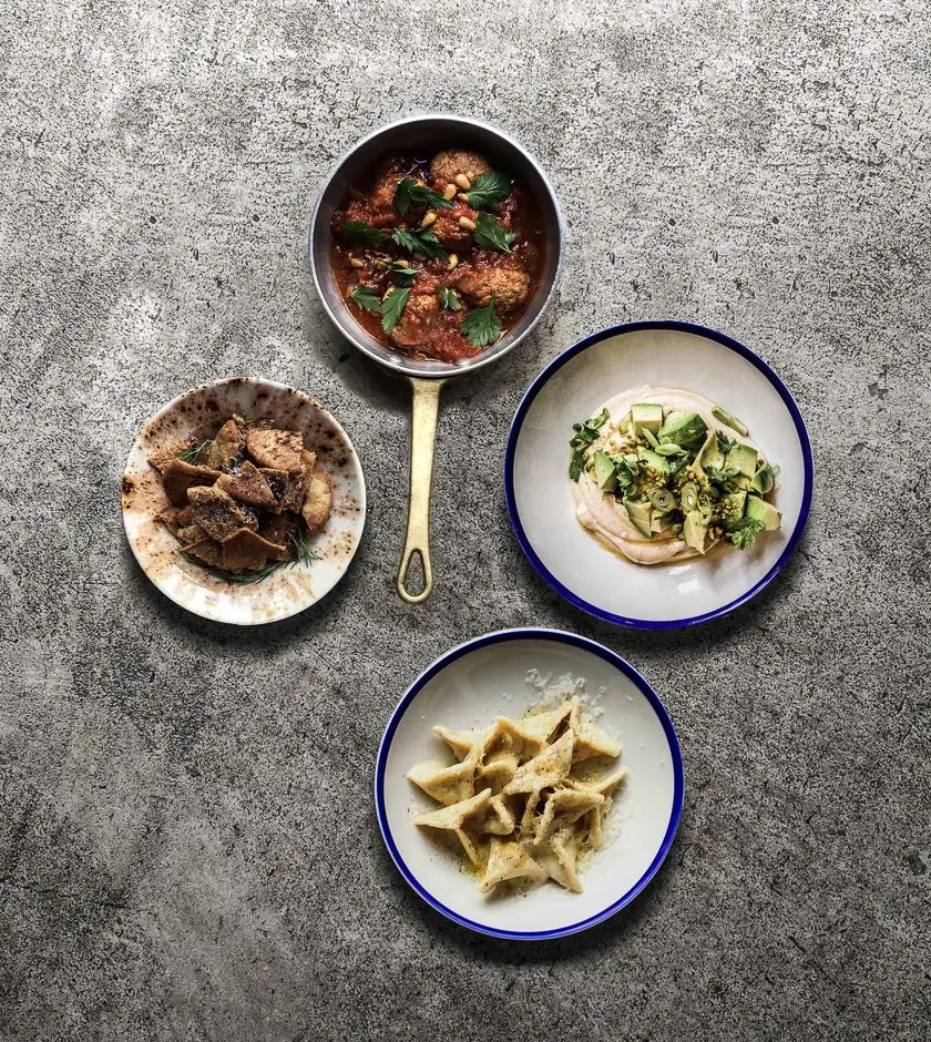 A spread of four small plates: braised meatballs in tomato sauce in a skillet, hummus with avocado and herbs, crispy pita chips, and a pasta dish, Bistrot Levante