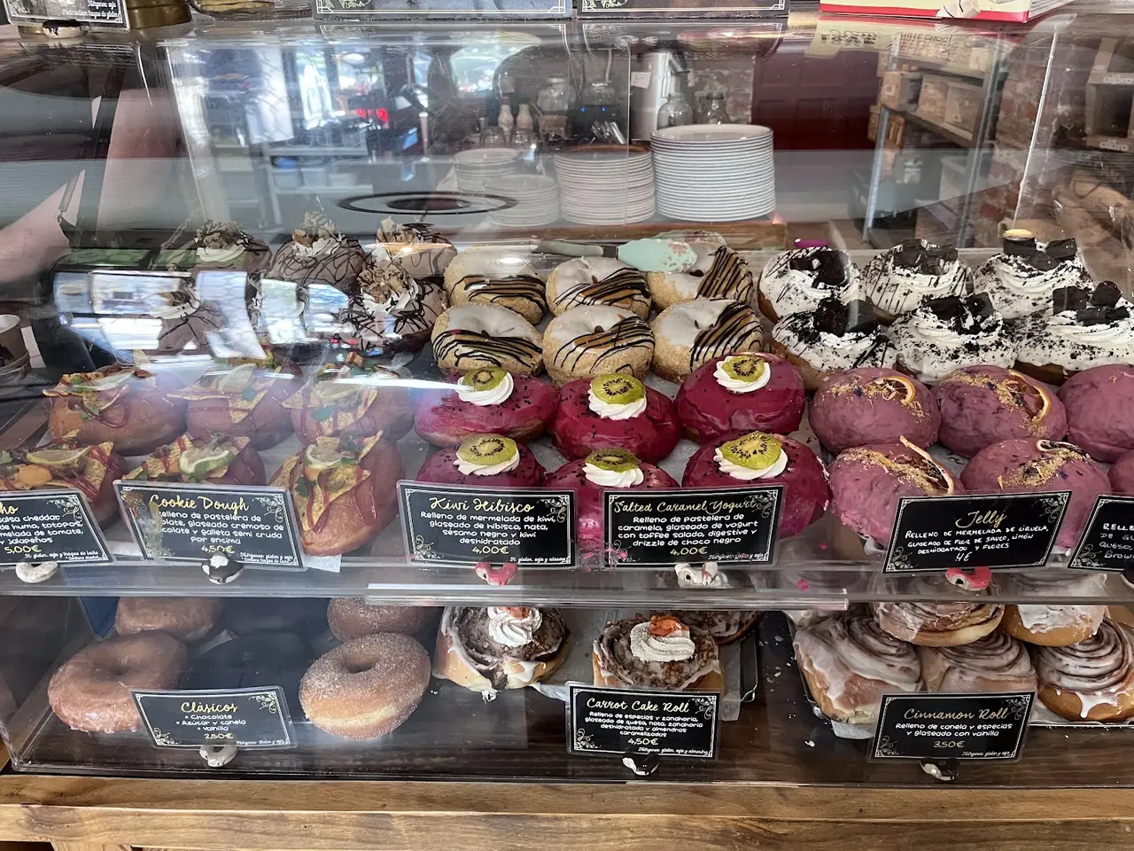 Bakery display case of assorted glazed and topped donuts, cinnamon rolls and carrot cake rolls