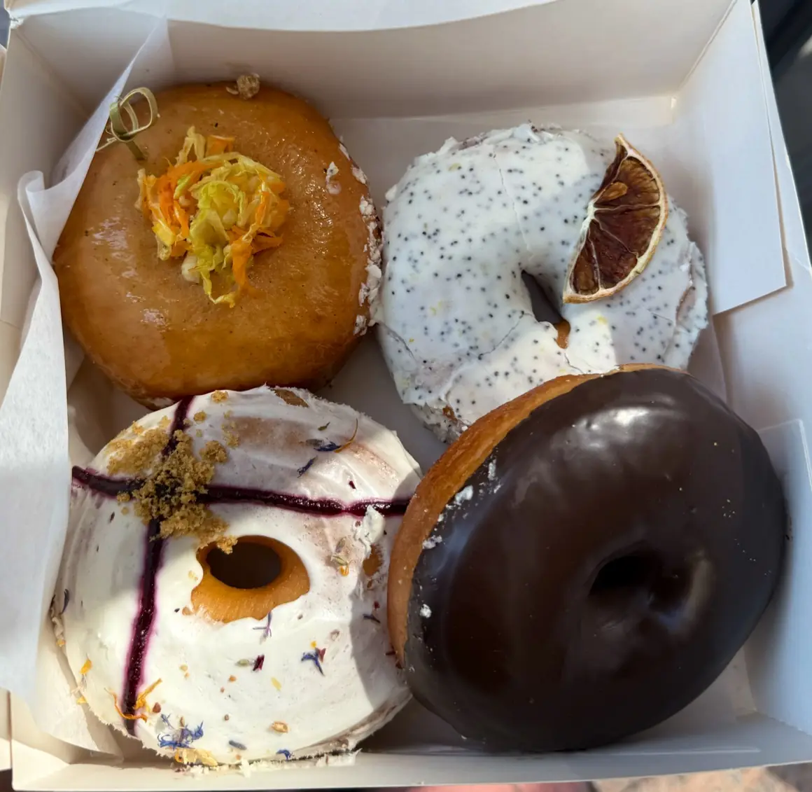 Box of four assorted glazed donuts including chocolate, poppy seed and floral toppings