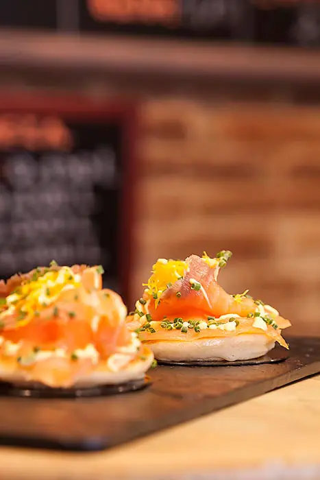 Small round bread bases topped with smoked salmon, chives, and citrus zest, at Blai 9