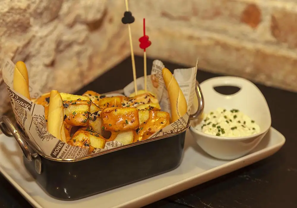 Patatas bravas with spicy sauce and chives in a metal dish lined with newspaper, served with bread and a bowl of aioli, at Blai 9