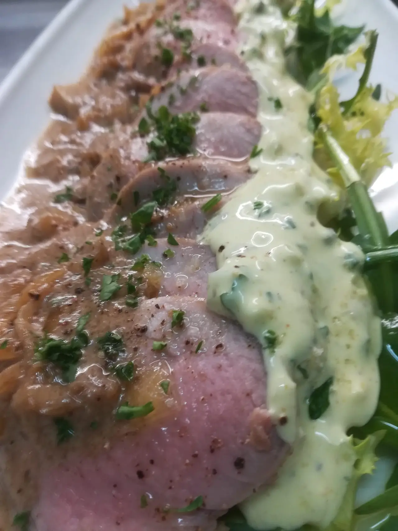 Sliced pork tenderloin in a brown mushroom sauce with chopped parsley, plated beside a creamy green herb sauce and frisée lettuce, at Blavis