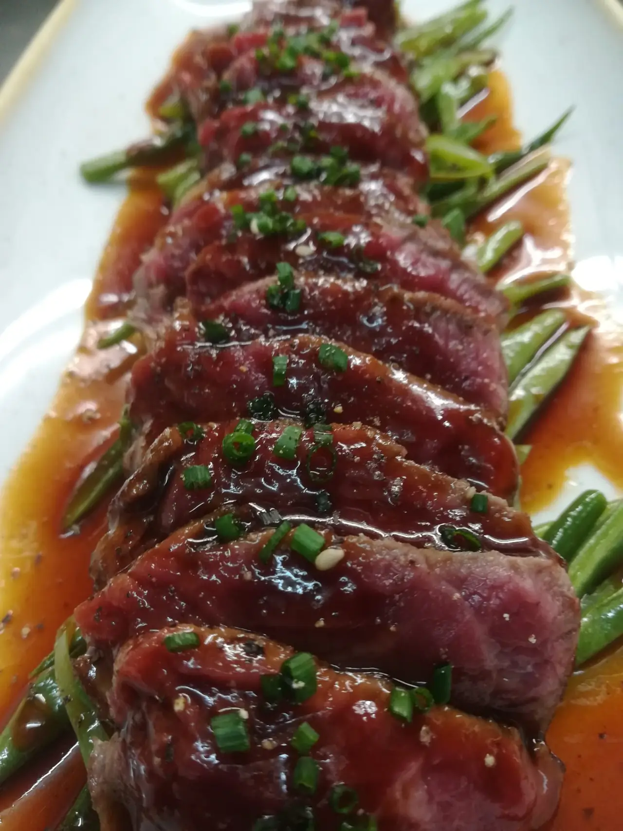 Sliced rare beef in a glossy red-brown sauce with chopped chives, served over green beans at Blavis