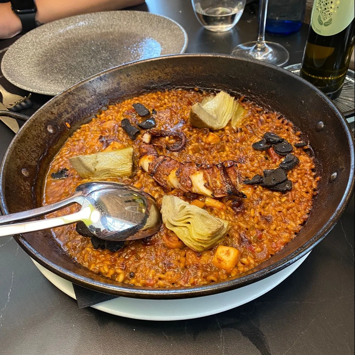 A pan of rice with artichokes and mushrooms and a serving spoon