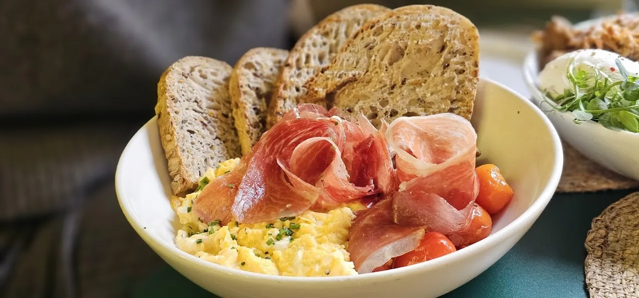 A bowl of scrambled eggs with prosciutto, cherry tomatoes, and toasted bread
