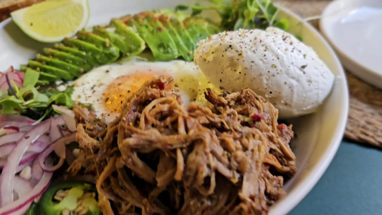A bowl with poached eggs, avocado, and shredded pulled meat