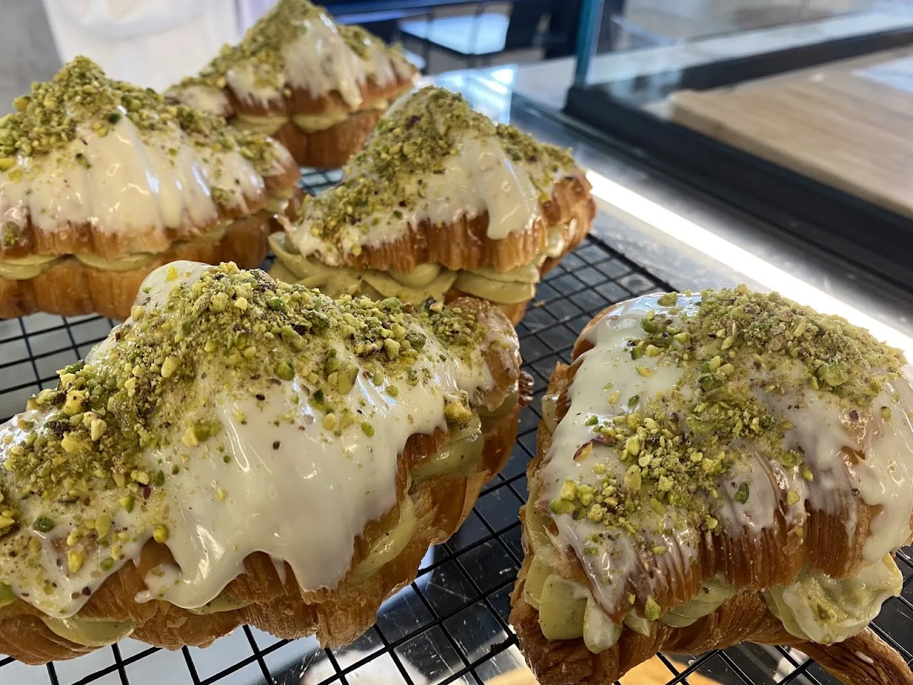 Pastries topped with pistachio and glaze on a cooling rack