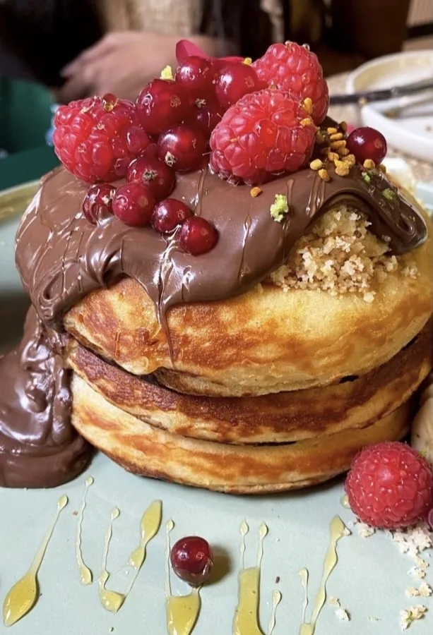A stack of pancakes topped with chocolate sauce and mixed berries