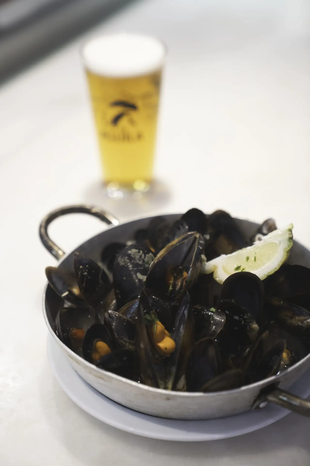 A copper pan of steamed mussels in their dark blue-black shells, garnished with a lime wedge and chopped herbs, at Bodega La Peninsular