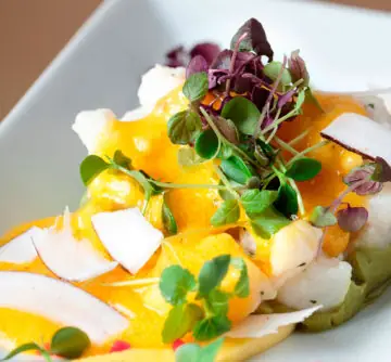 Overhead plate of white fish carpaccio draped in bright orange sauce, topped with microgreens and herbs
