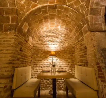 Intimate vaulted brick alcove with a single table for two lit by a shaded lamp, cream banquette seating