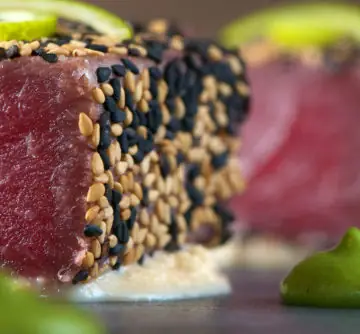Close-up of a seared red tuna cube crusted in toasted white and black sesame seeds over pale sauce
