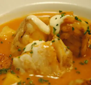 Bowl of fish stew in saffron-orange broth with chunks of white fish, mayonnaise dollops and chopped chives