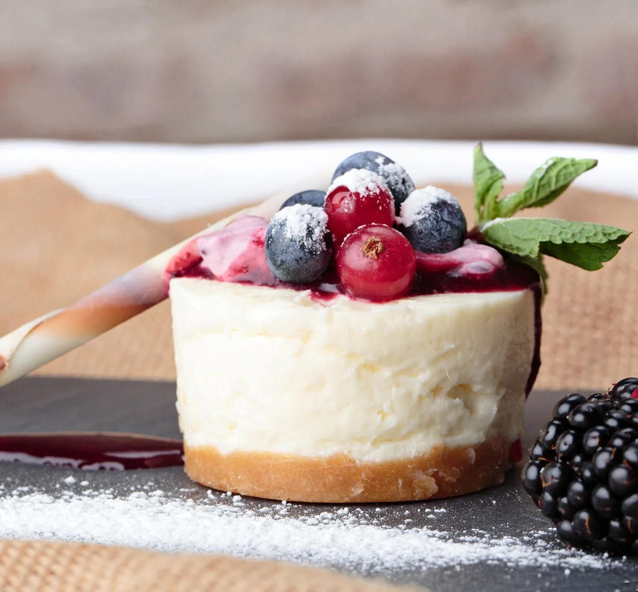 A small round cheesecake topped with berries and mint on a slate board