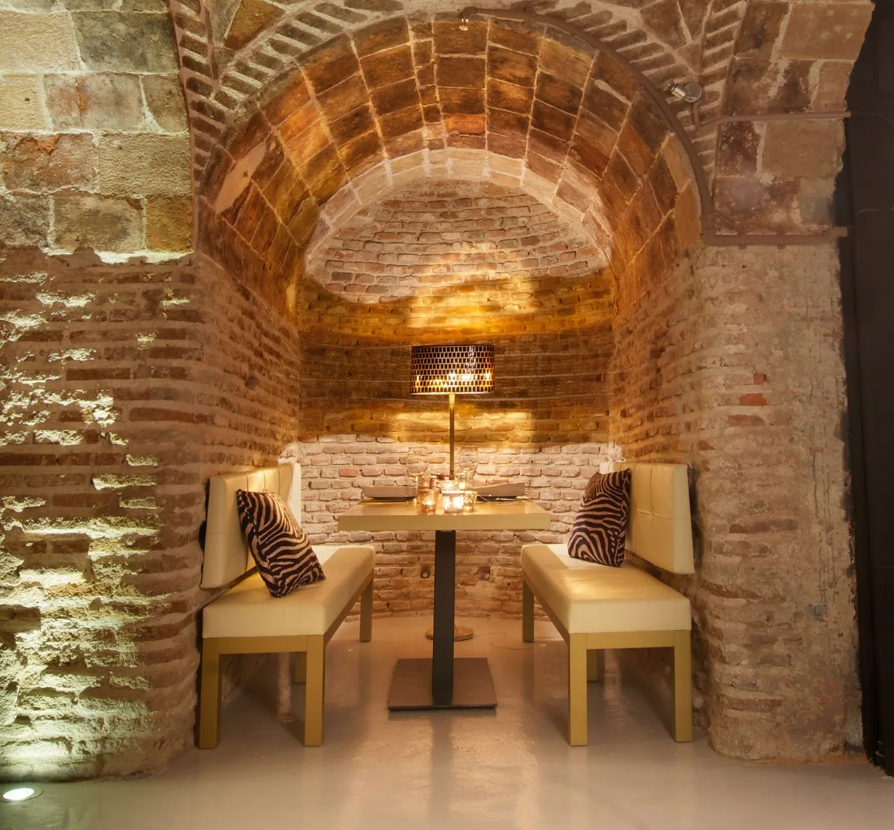 A cream bench and set table in a brick vaulted room with patterned cushions